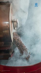 Light smoke and coffee roasting fumes rising from a coffee roasting machine during the roasting process.