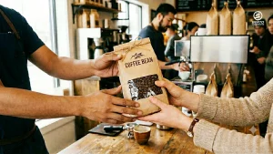 The hands of two people exchanging a paper bag of coffee beans.